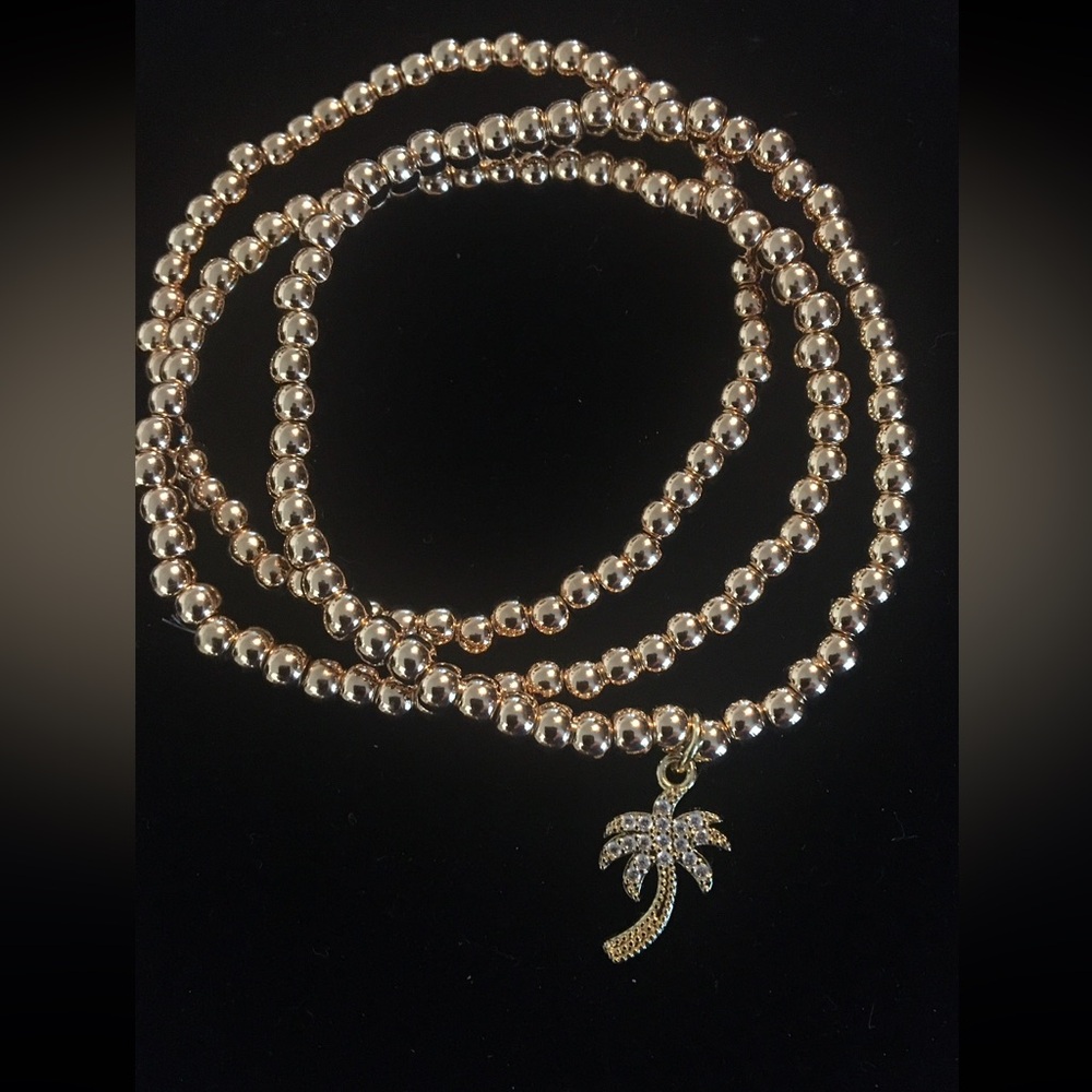 Three Gold Stretch Beaded Bracelets-one with a crystal Palm Tree Charm. Fits all